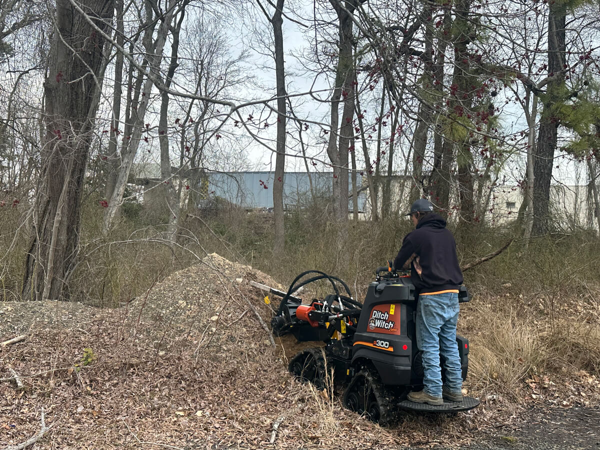 A man operating ditch witch machine on a pile of garbage